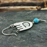 Mexican silver bird earring with a turquoise bead on a dark surface