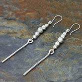 Silver dangly earrings with beads on a stone surface