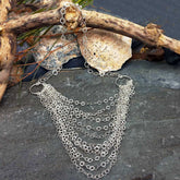 Silver chain necklace on a stone surface with a piece of driftwood.
