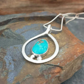 Silver pendant with a turquoise stone on a stone surface