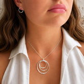 Silver necklace with a circular pendant on a person wearing a white shirt.