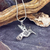 A sterling silver hummingbird pendant necklace with floral and dotted details, hanging from a silver chain.