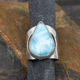 Teardrop-shaped larimar stone ring on a dark stone background