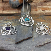 Three silver pendants with gemstones on a stone surface