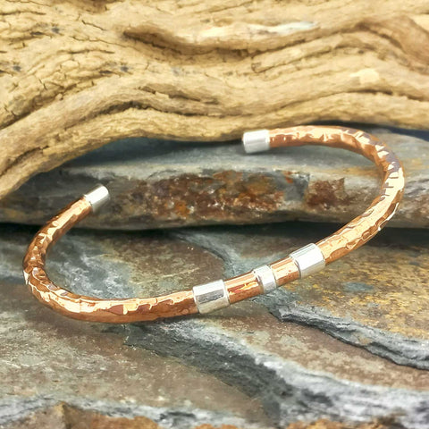 An artisanal hammered copper bangle bracelet with silver end caps and spacer beads.