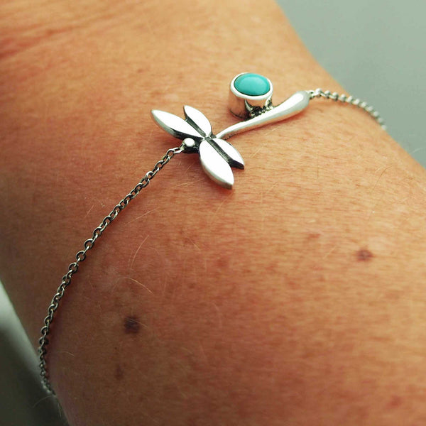 A silver bracelet with a dragonfly design and a turquoise stone on a person's wrist.