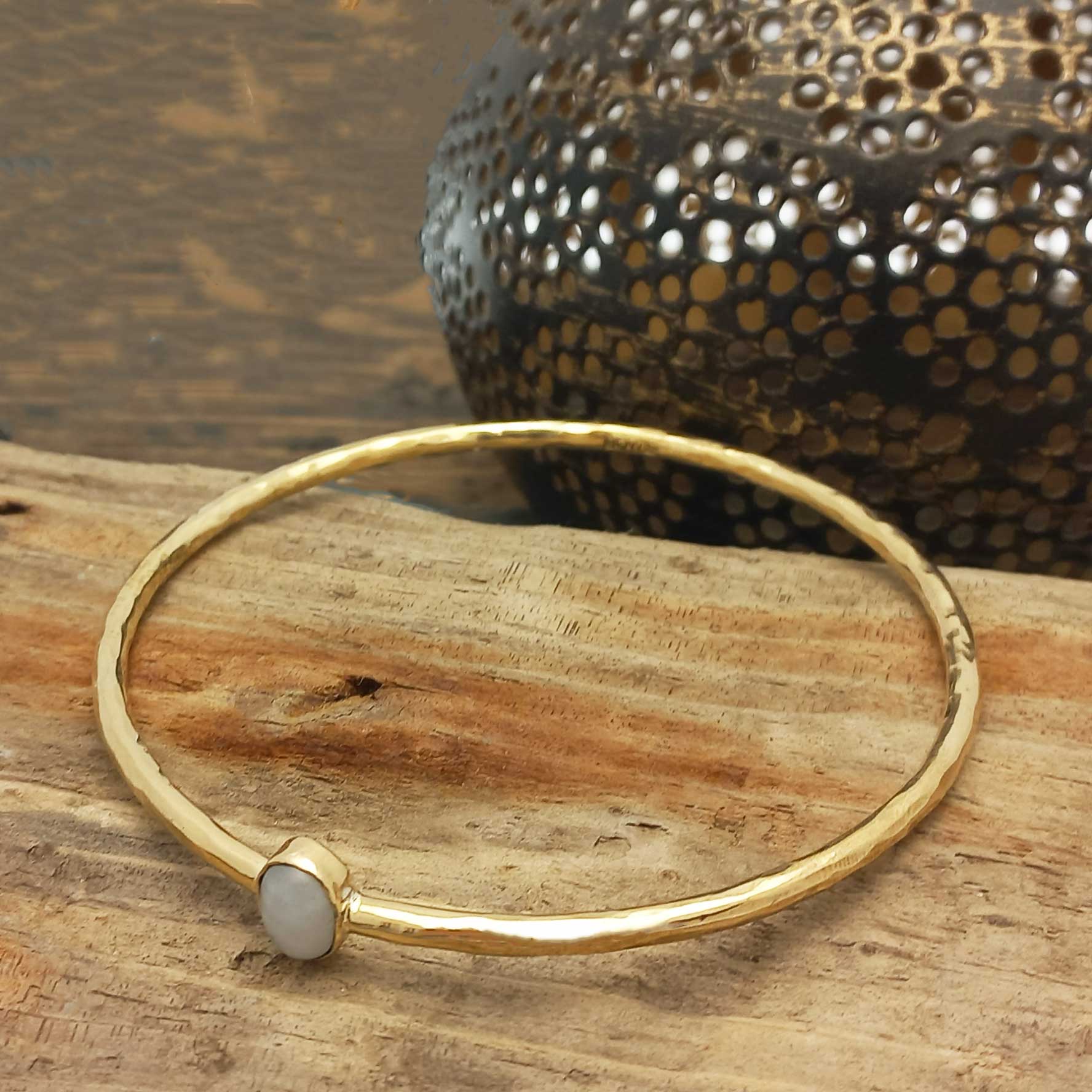 Gold coloured brass bracelet with a moonstone stone on a wooden surface with a textured object in the background.
