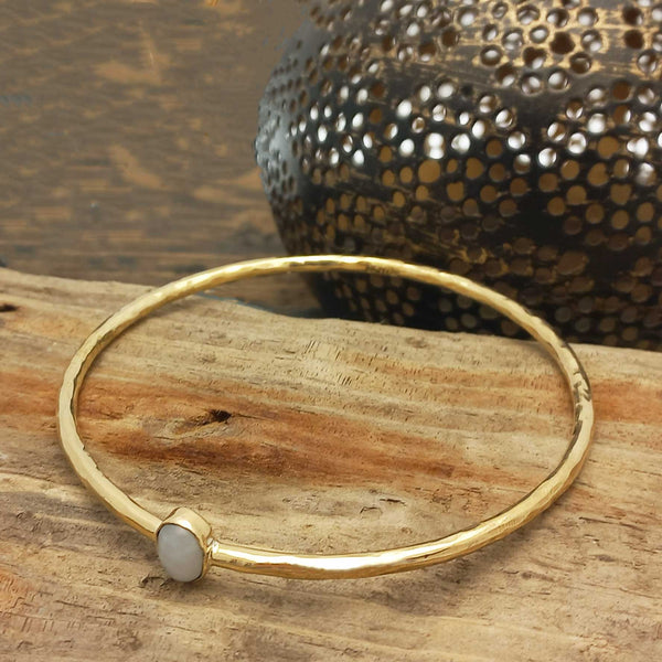 Gold coloured brass bracelet with a moonstone stone on a wooden surface with a textured object in the background.
