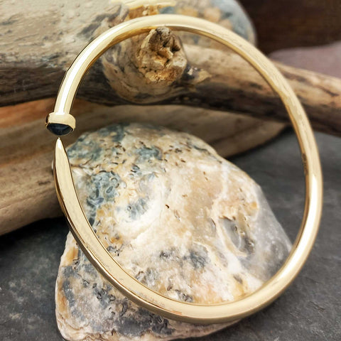 Gold bracelet with a gemstone on a stone surface with wooden elements in the background