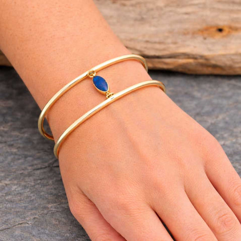 Gold coloured brass bracelet with a blue Lapis stone on a wrist against a wooden background