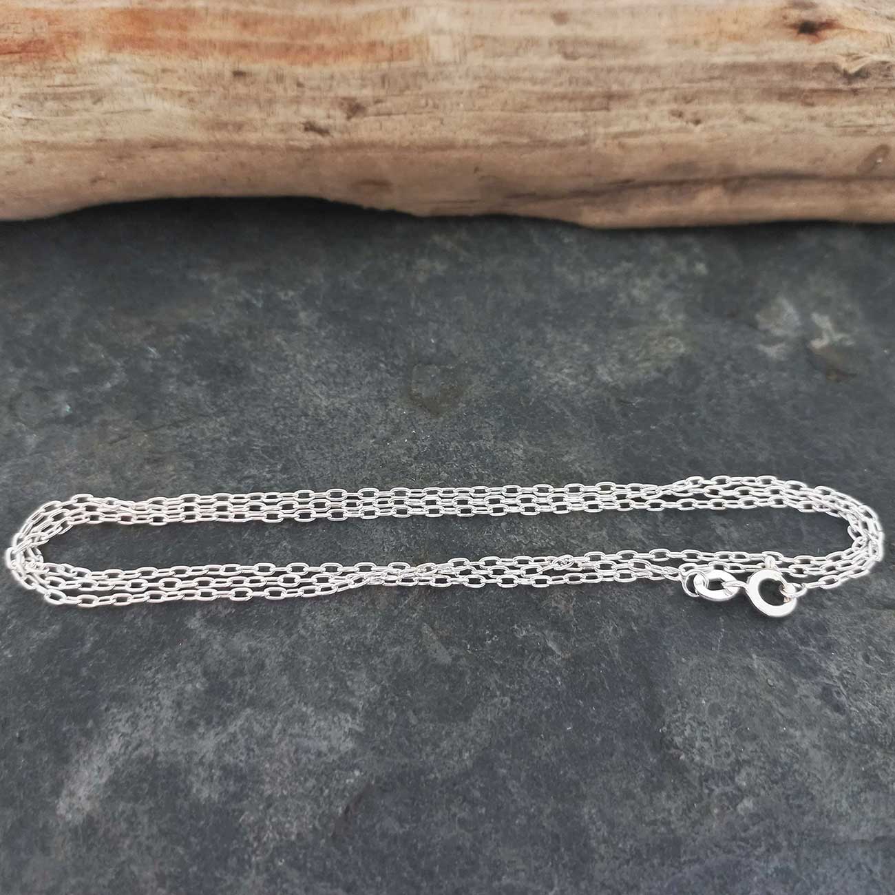 Silver chain on a dark stone surface with a wooden log in the background