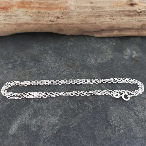 Silver chain on a dark stone surface with a wooden log in the background