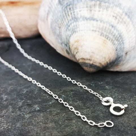 Silver chain necklace on a dark stone surface with a shell in the background