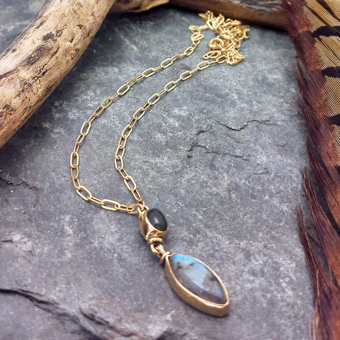 Gold coloured brass necklace with Labradorite pendant on a stone surface