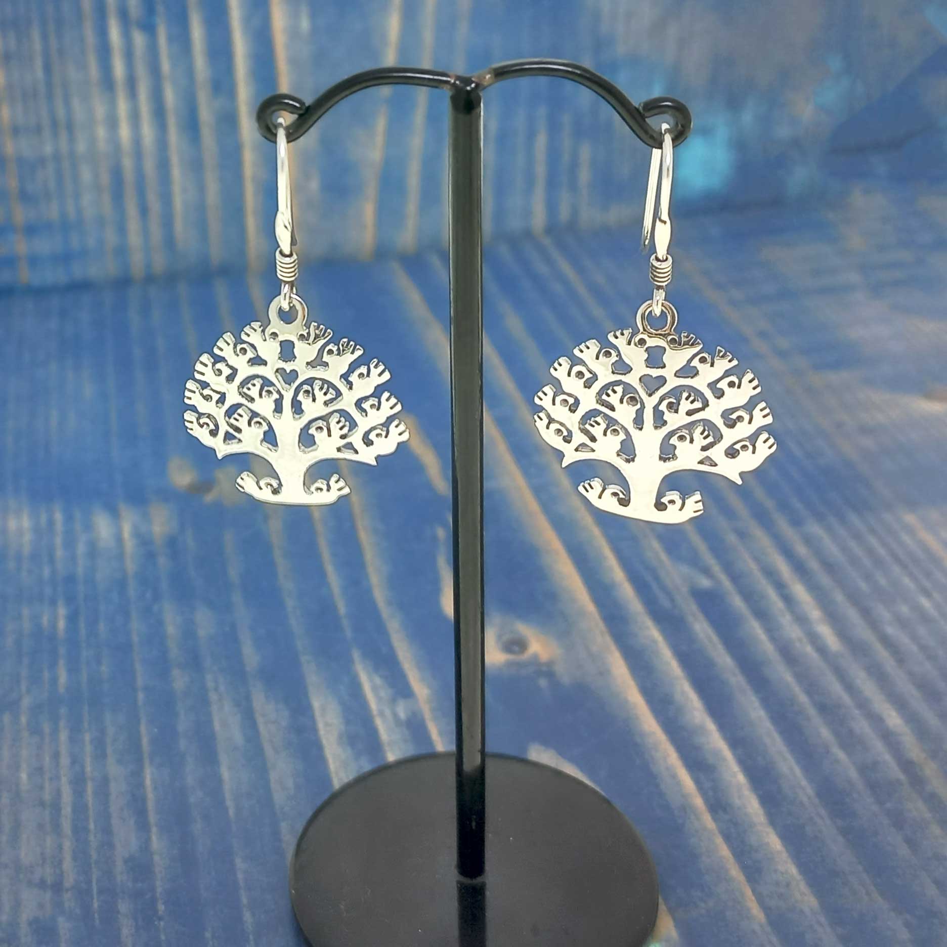 Silver tree-shaped unusual earrings on a black stand against a blue textured background