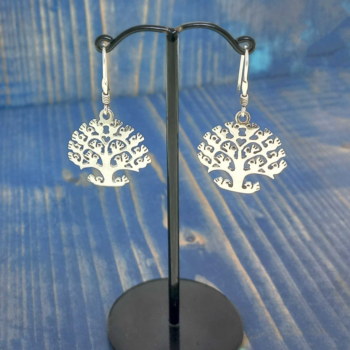 Silver tree-shaped unusual earrings on a black stand against a blue textured background