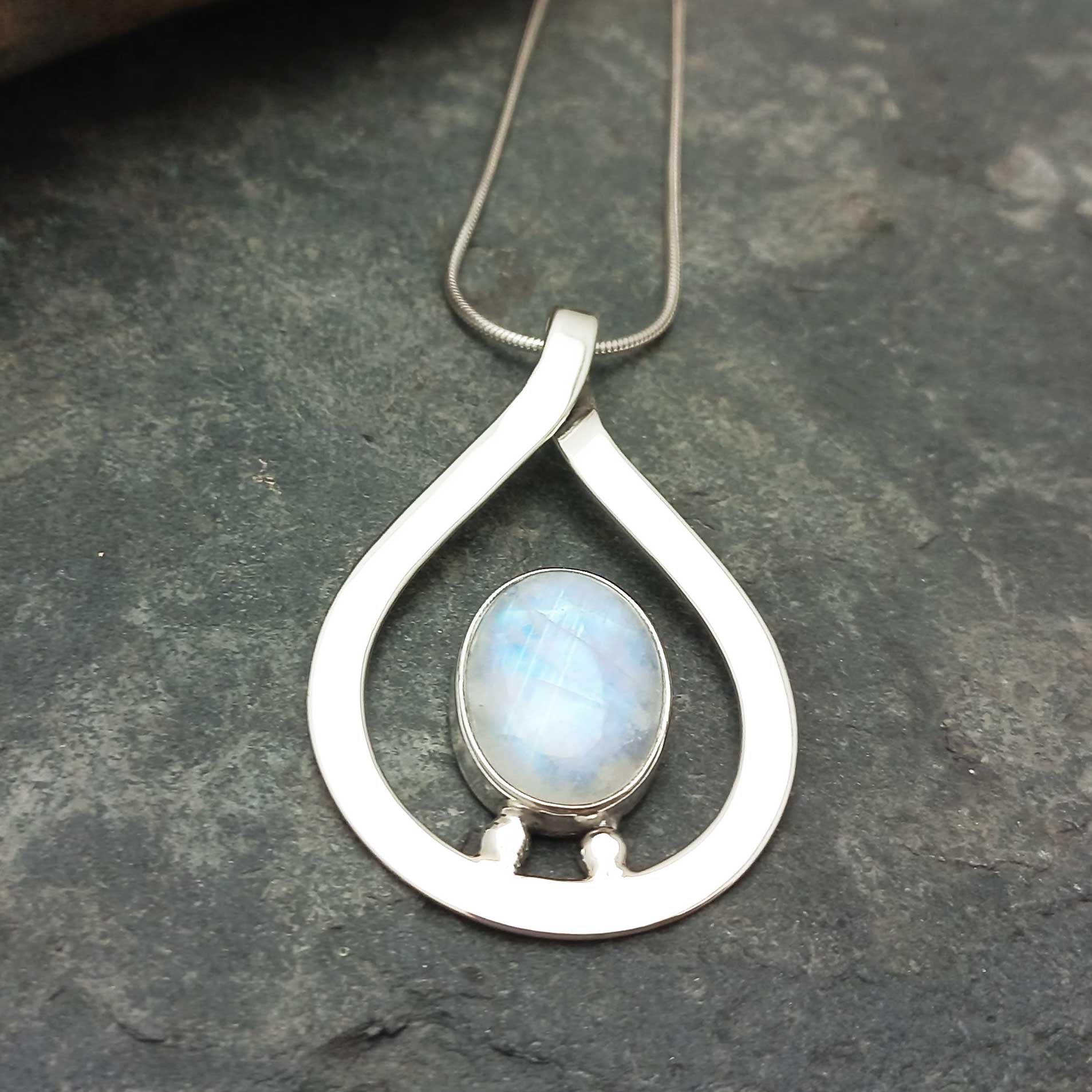 Teadrop handcrafted silver pendant with a moonstone on a dark stone surface
