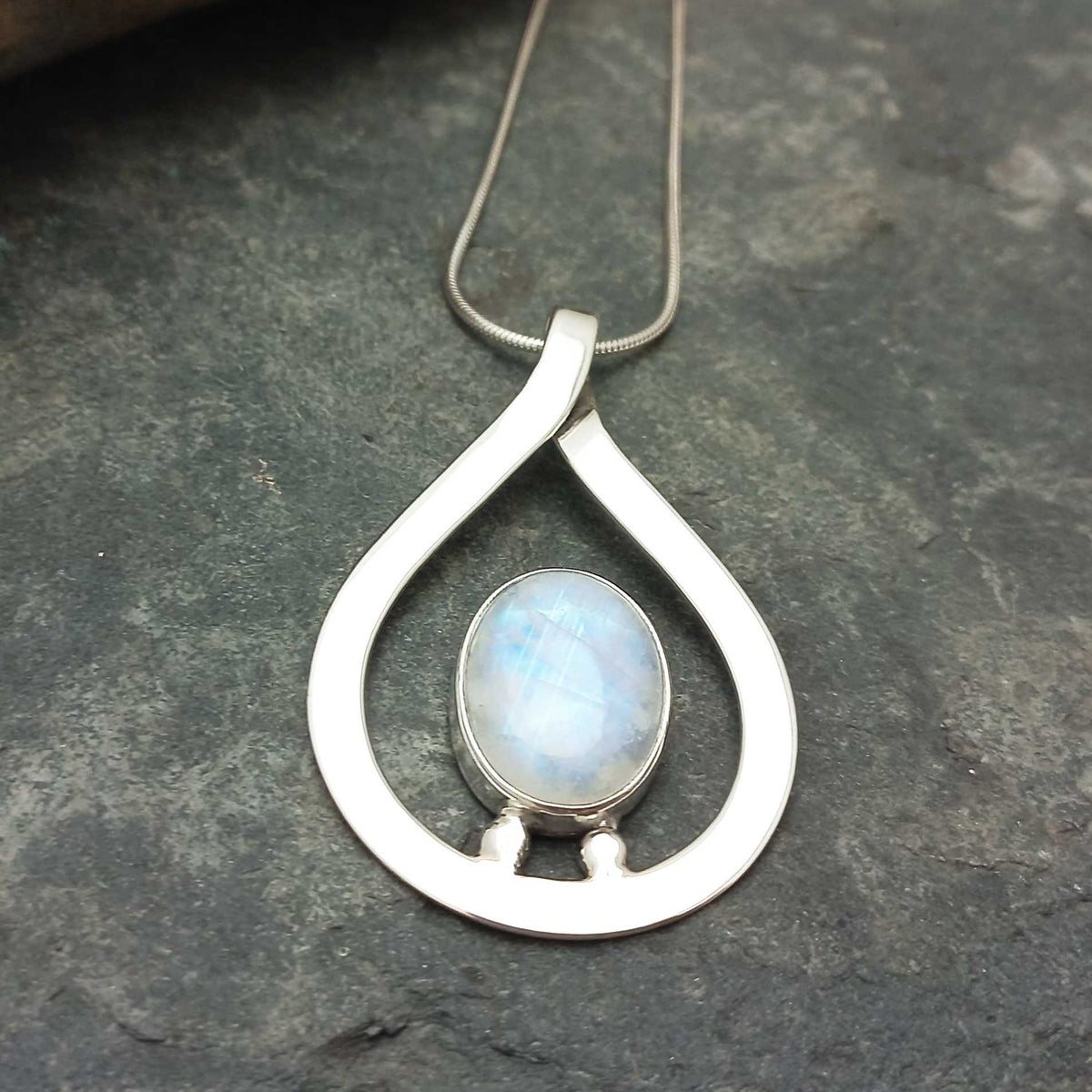 Teadrop handcrafted silver pendant with a moonstone on a dark stone surface