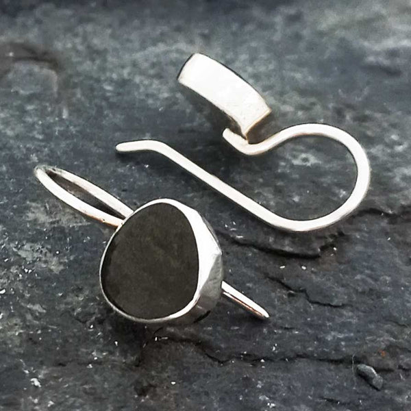 Silver earrings with black Obsidian stone on a dark stone surface