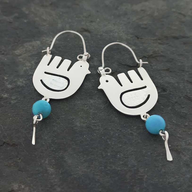 Pair of silver dove-shaped earrings with turquoise beads on a dark stone background