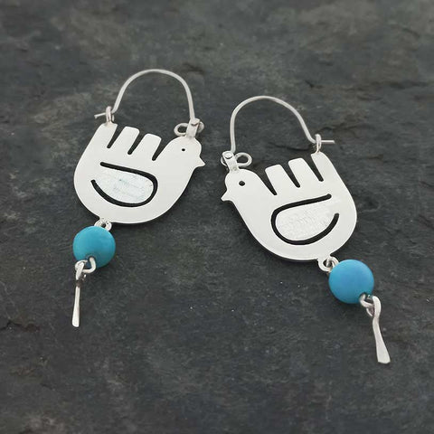 Pair of silver dove-shaped earrings with turquoise beads on a dark stone background