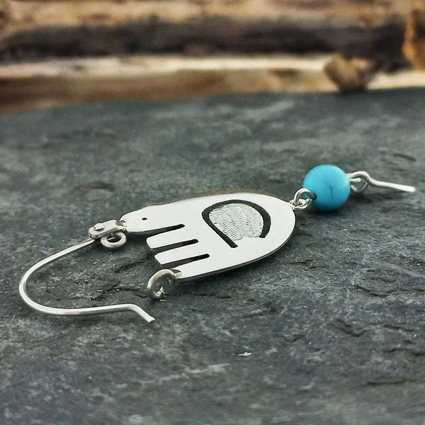 Mexican silver bird earring with a turquoise bead on a dark surface
