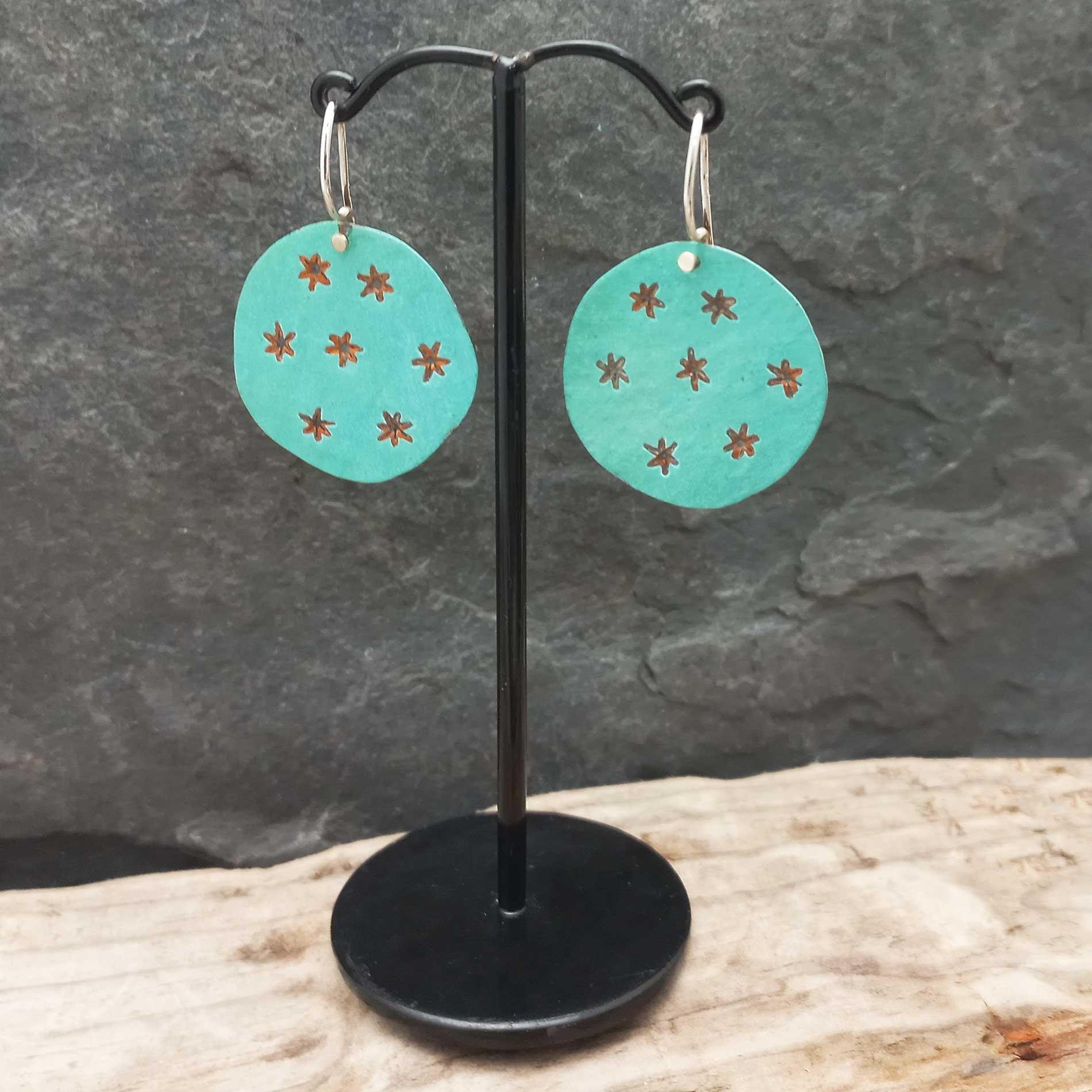 Turquoise earrings with star patterns on a black stand against a stone background