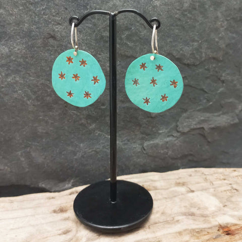 Turquoise earrings with star patterns on a black stand against a stone background