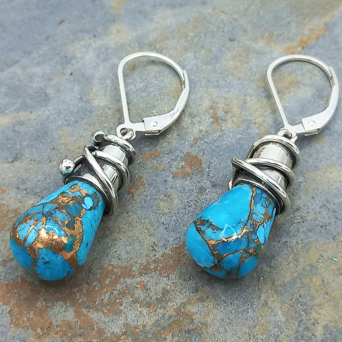 Pair of turquoise stone earrings with silver and gold accents on a stone surface