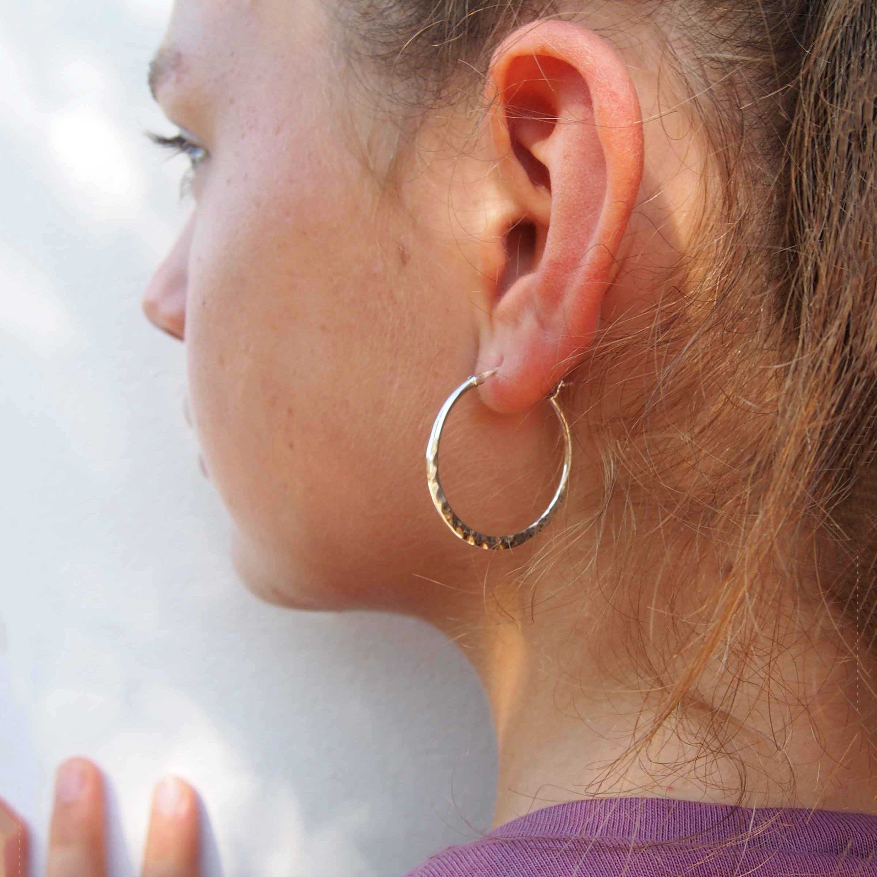 Close-up of a person wearing a silver hoop earring against a white background