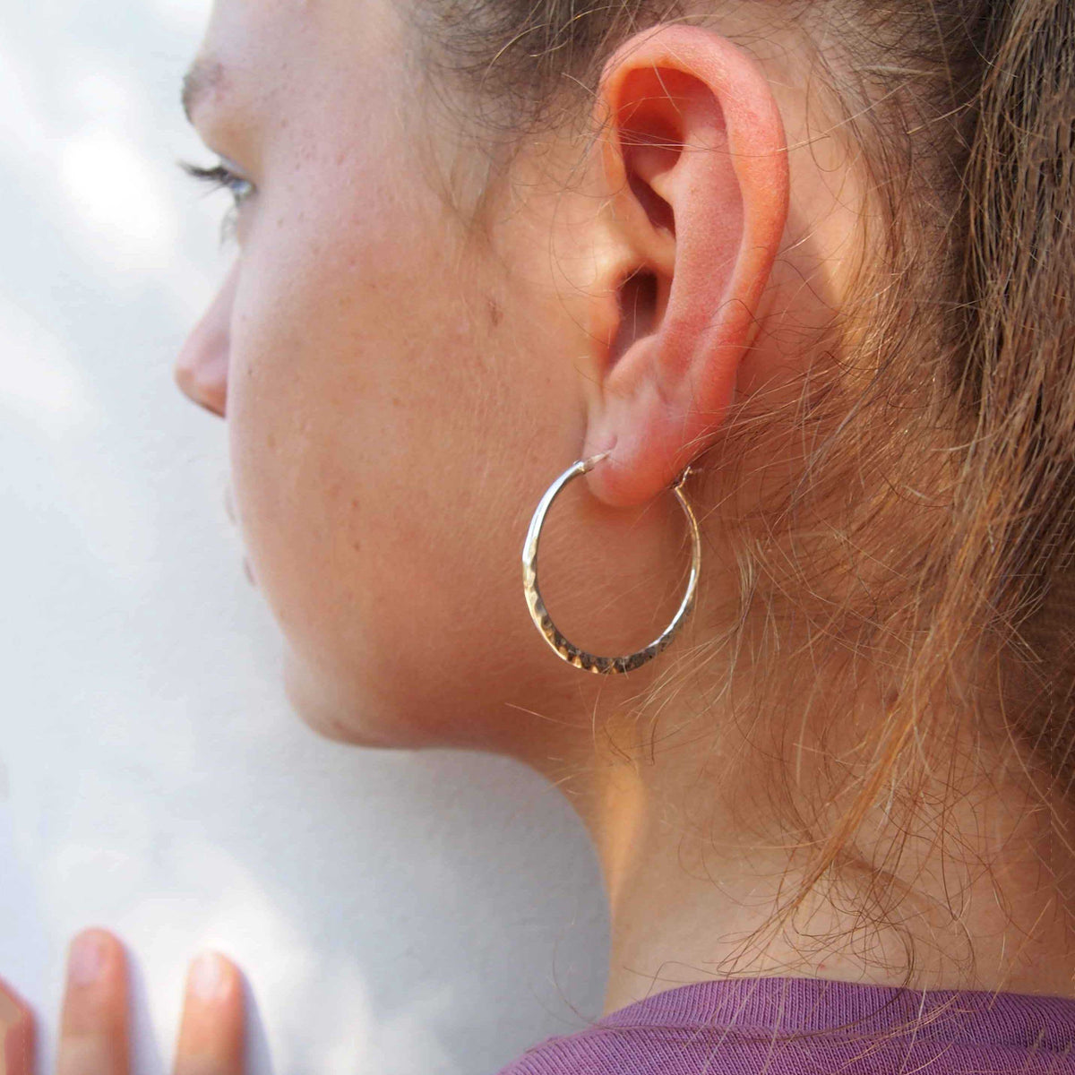 Close-up of a person wearing a silver hoop earring against a white background