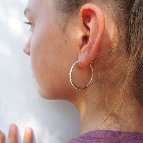 Close-up of a person wearing a silver hoop earring against a white background