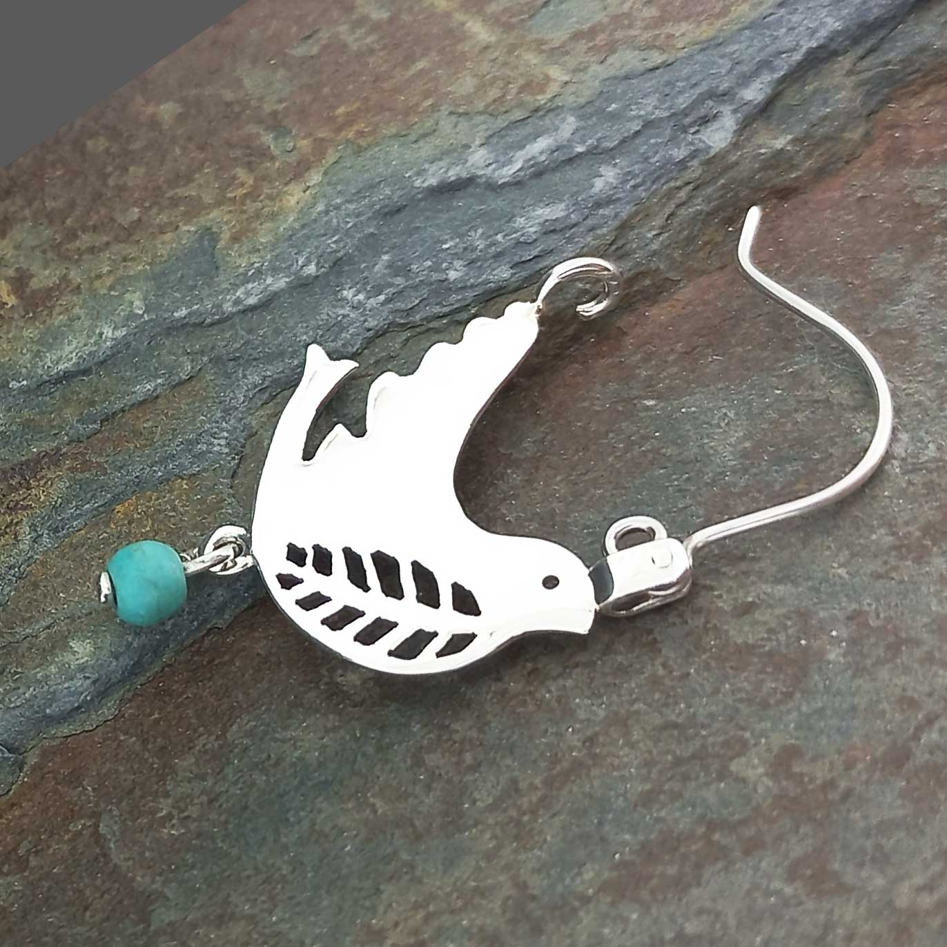 A sterling silver earring featuring a cutout bird silhouette charm with a small turquoise bead 