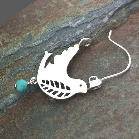A sterling silver earring featuring a cutout bird silhouette charm with a small turquoise bead 