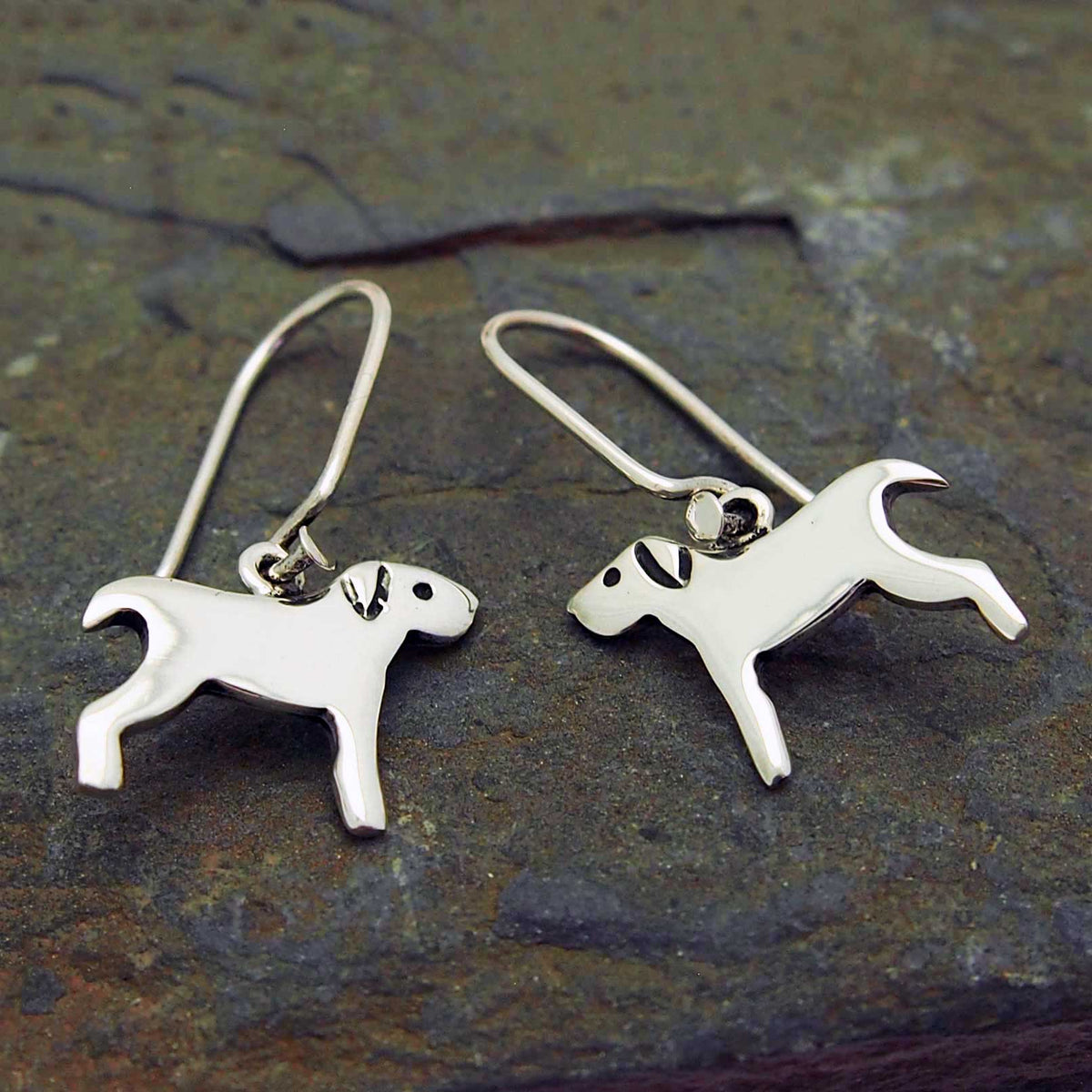 Silver dog-shaped earrings on a textured stone surface
