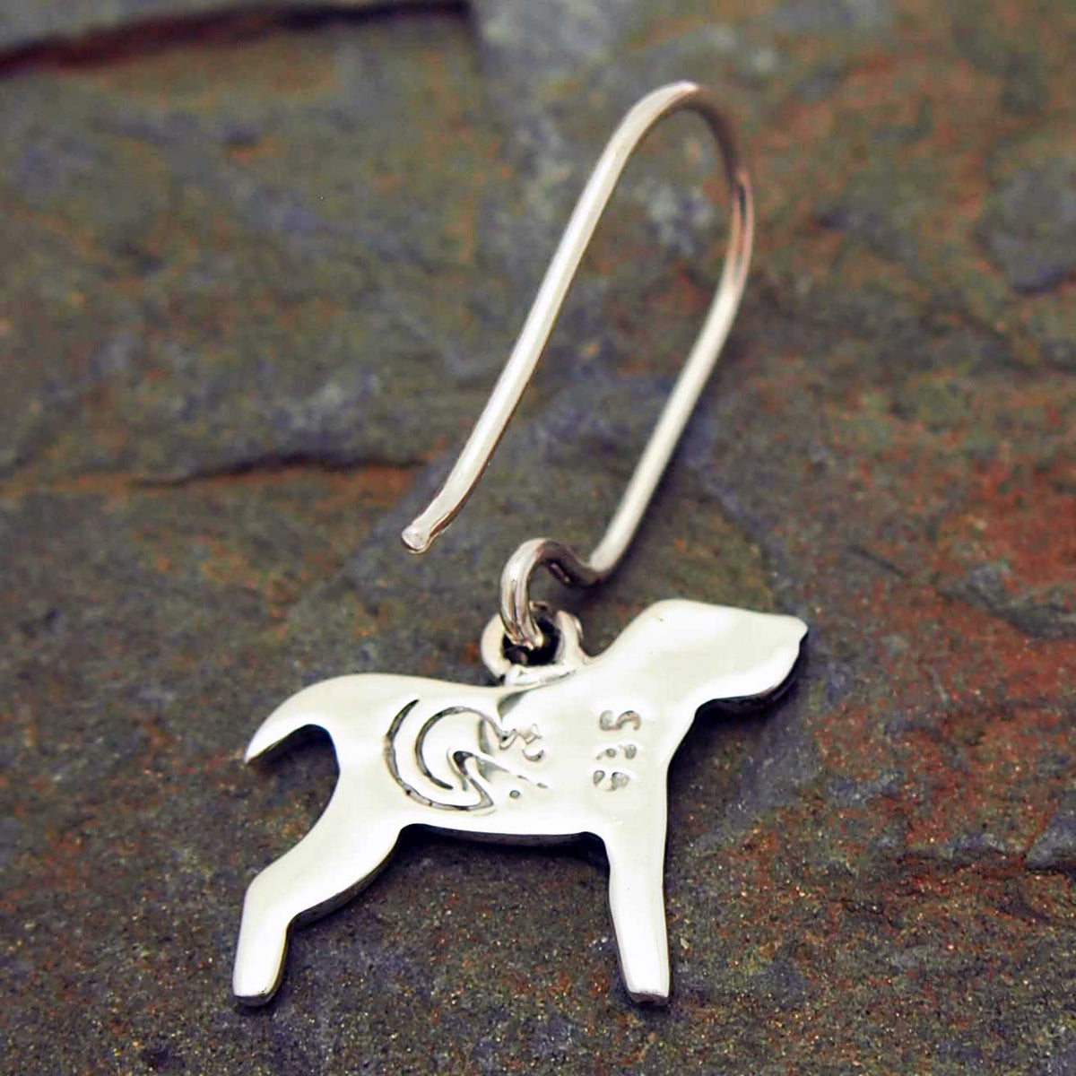 Back of silver dog-shaped earring on a textured stone surface