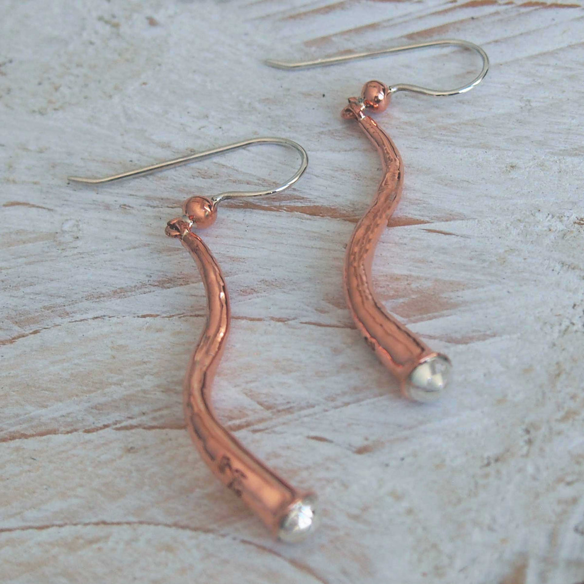 Copper earrings with a wavy design on a light wooden surface