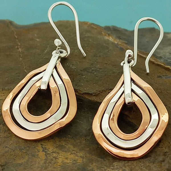 Pair of earrings with layered copper and silver design on a stone surface