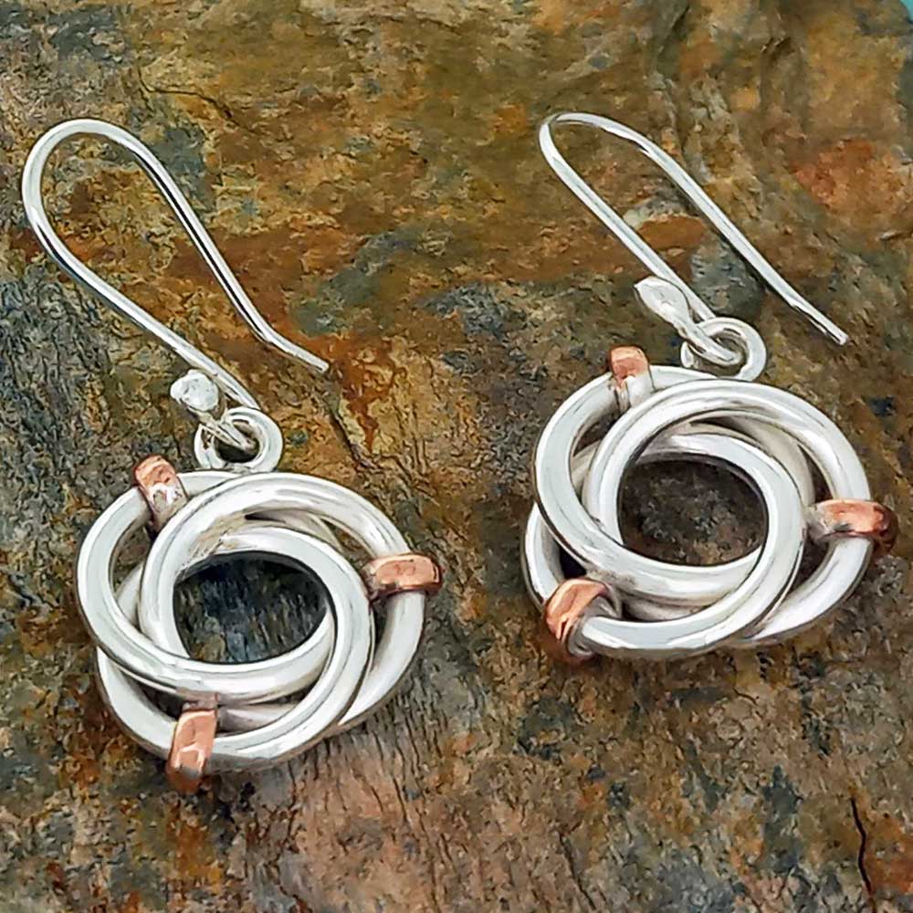 Pair of silver and copper earrings on a stone surface Main image