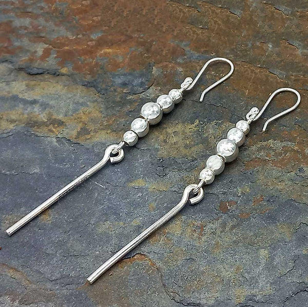 Silver dangly earrings with beads on a stone surface