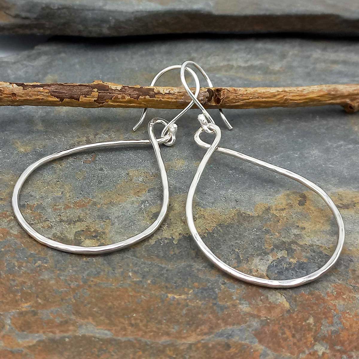 Silver drop hoop earrings on a stone surface with a branch