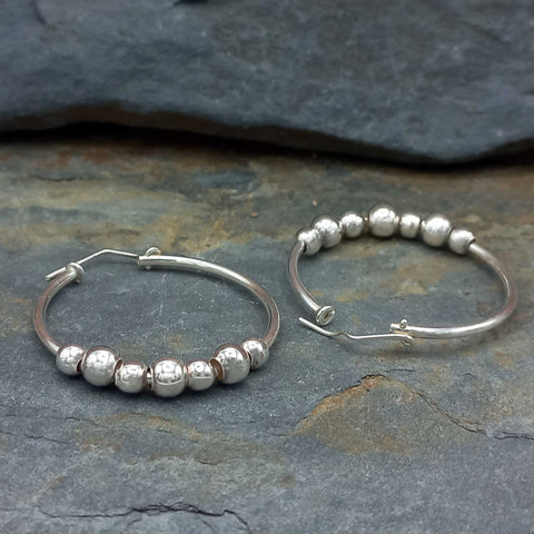 Silver hoop earrings with bead detailing on a stone surface