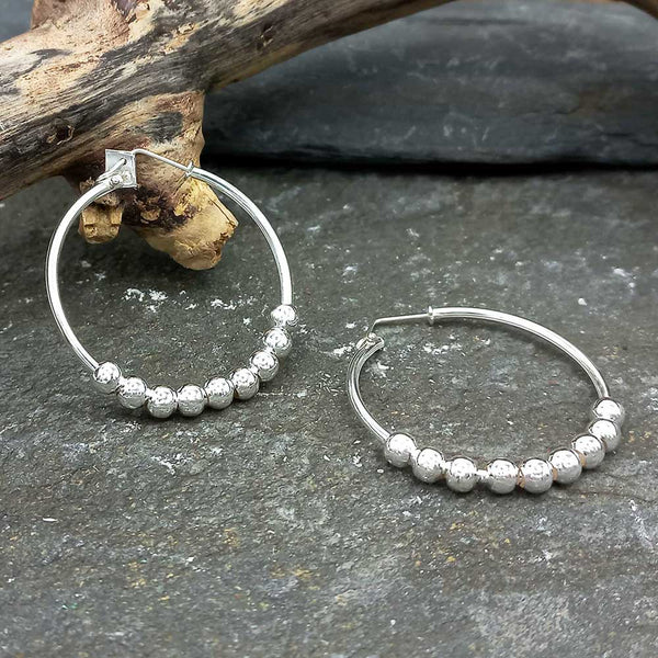 Silver hoop earrings with bead detailing on a stone surface