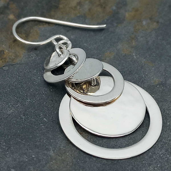 Silver earrings with circular designs on a dark stone surface