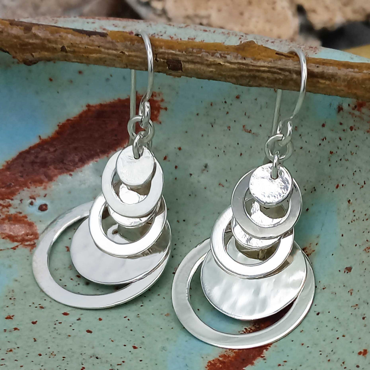 Silver circular earrings hanging on a rustic metal surface. Main image
