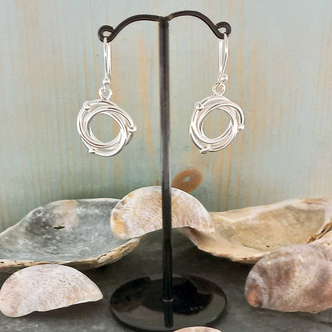 Silver earrings on a stand with seashells in the background
