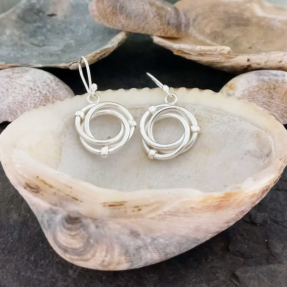 Handmade silver earrings on a shell with a natural background