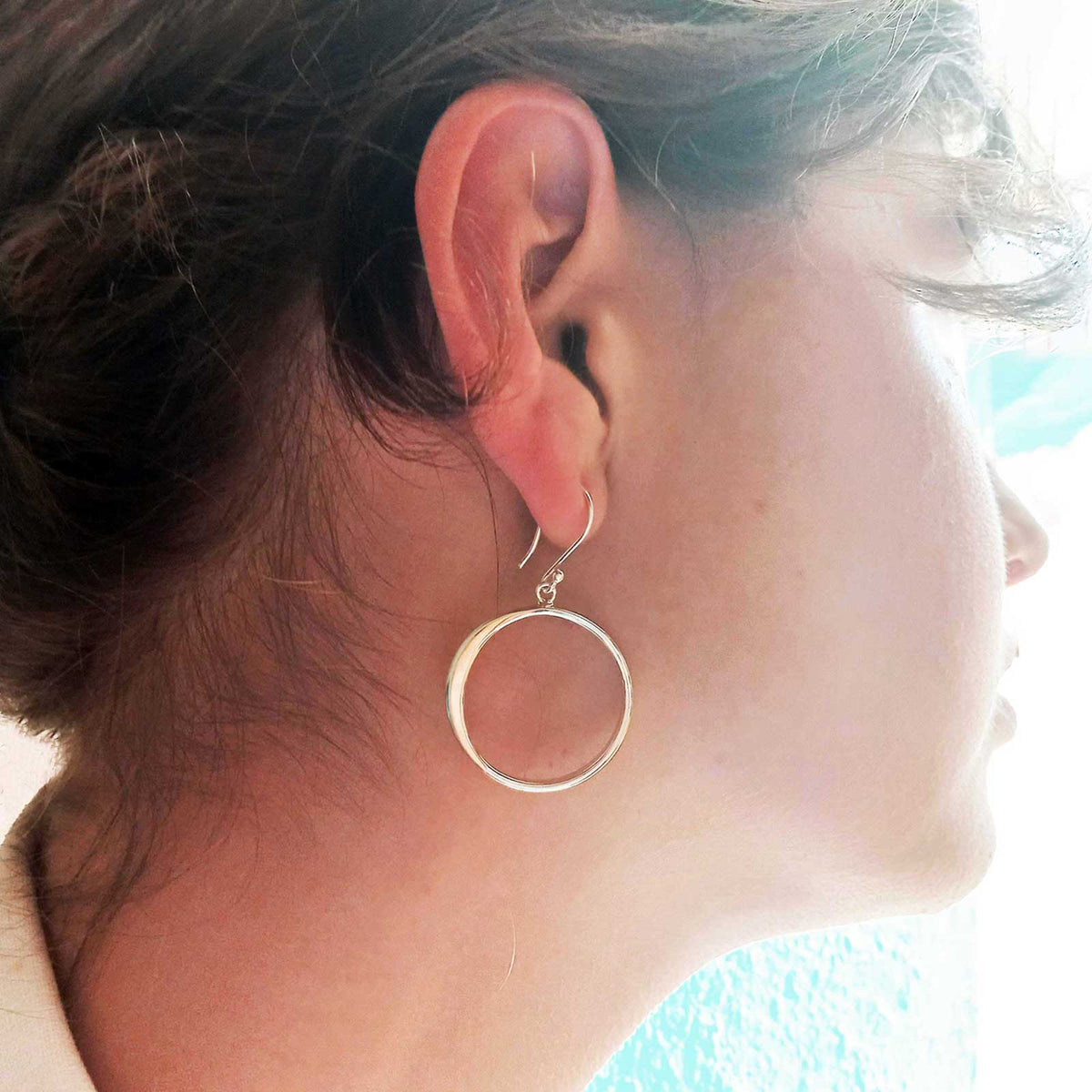 Close-up of a person wearing a silver circle earring with a blurred background