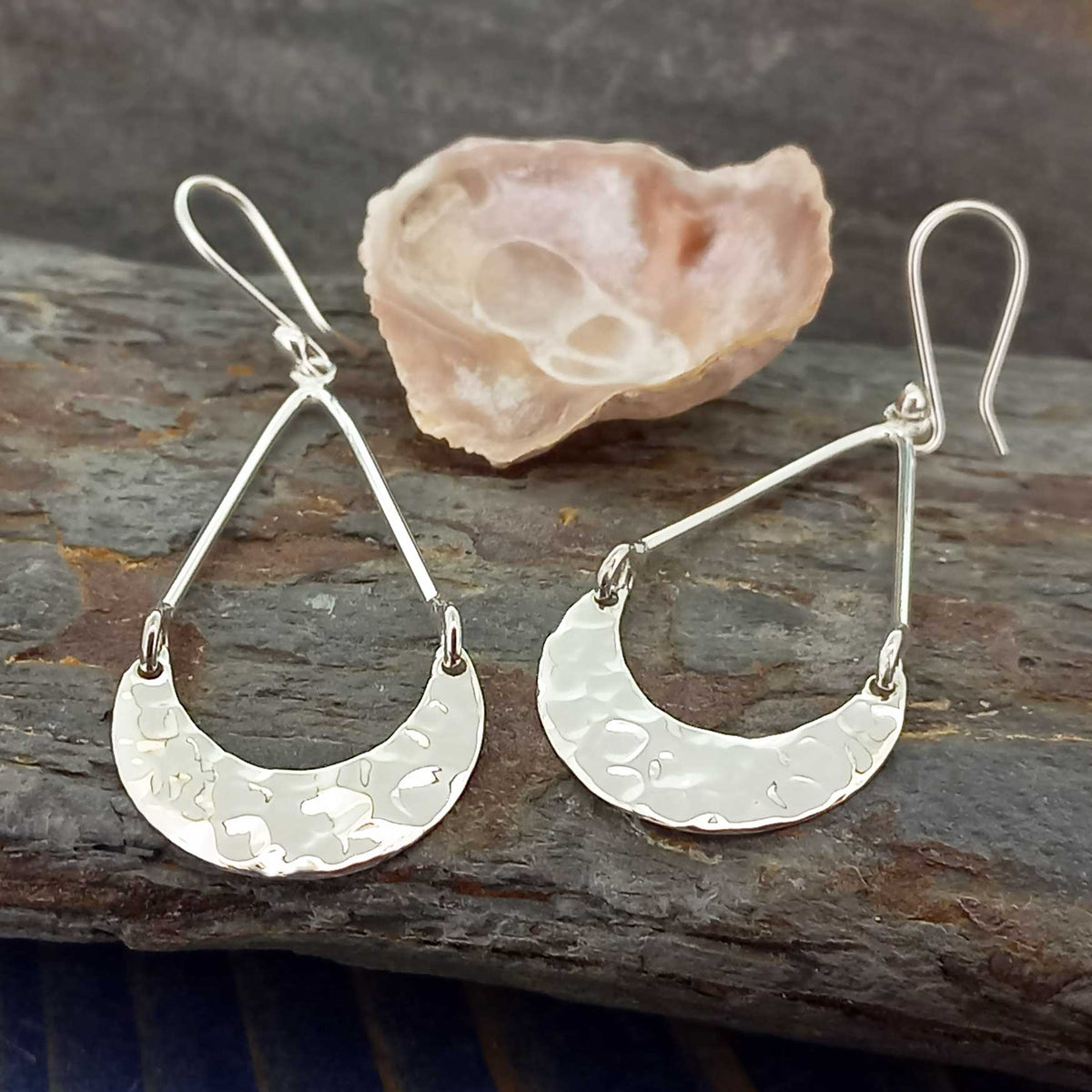 Silver earrings with crescent moon design on a stone surface Main image