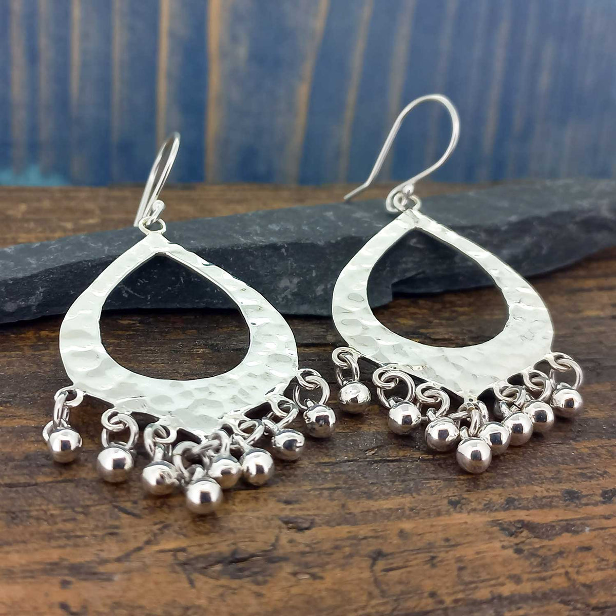 Pair of silver hammered hoop earrings with dangling beads on a wooden surface.